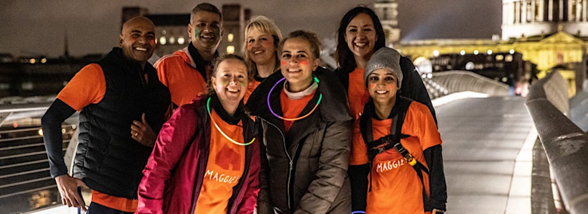 Group of friends on night hike along the Thames with London landmarks lit up in background