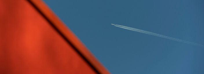 Abstract photo of orange roof of Maggie's West London and blue sky with plane flying over